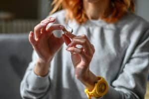 Young redhead woman holding hearing aid in her hands