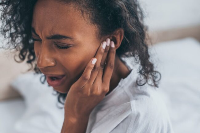 young african american woman suffering from ear pain in bedroom with closed eyes What are some signs of hearing loss?