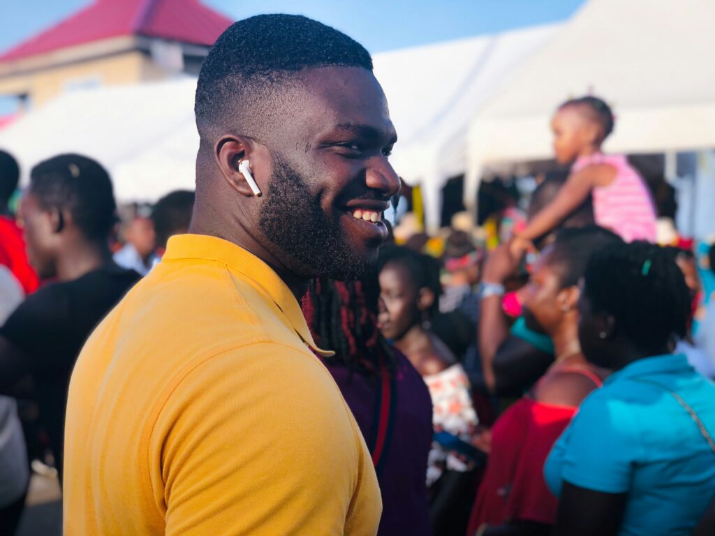 A casually dressed black man in a crowd with an Apple AirPod in one ear.