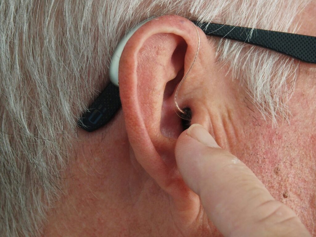 the ear of a man with black glasses touching his ear with a hearing aid.