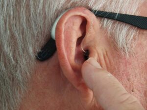 the ear of a man with black glasses touching his ear with a hearing aid.