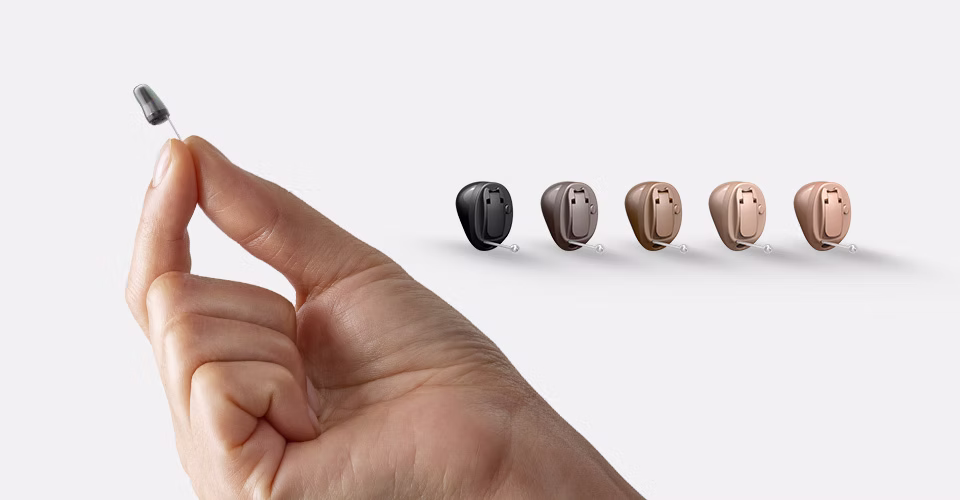 A hand holding the Oticon OWN SI hearing aid with additional examples of colorways.