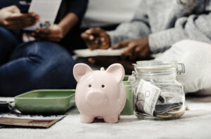 A pink piggy bank sitting next to a jar filled with money in front of two people filling out paperwork.