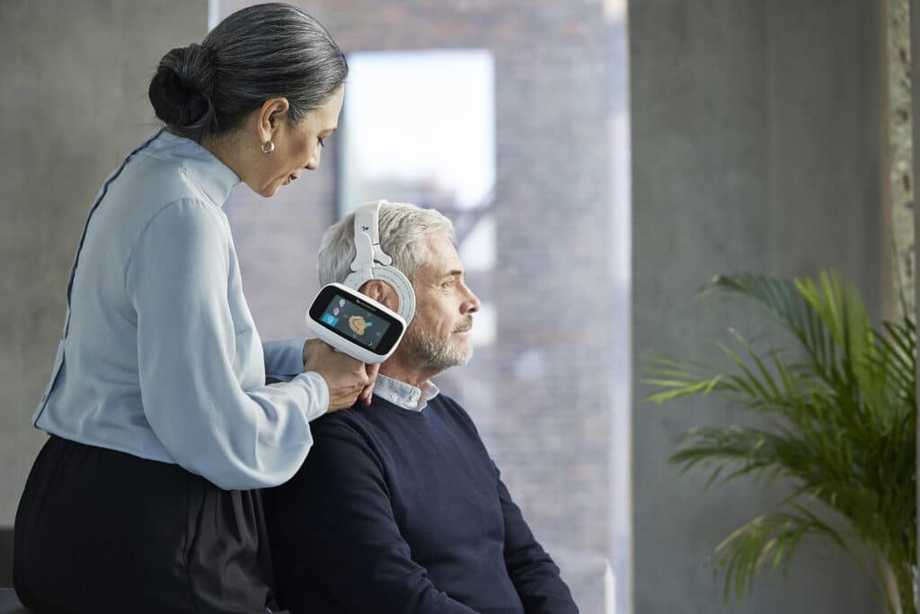 a female audiologist using the Otoscan 3D digital scanner to map the shape of an older man's right ear.