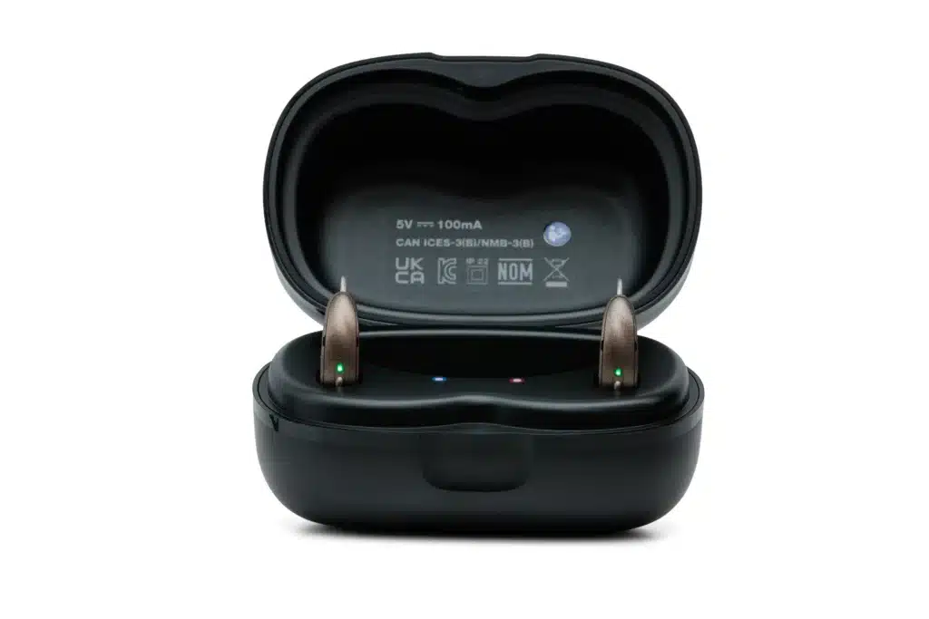 A pair of beige Starkey Omega AI hearing aids in their black rechargeable storage case.